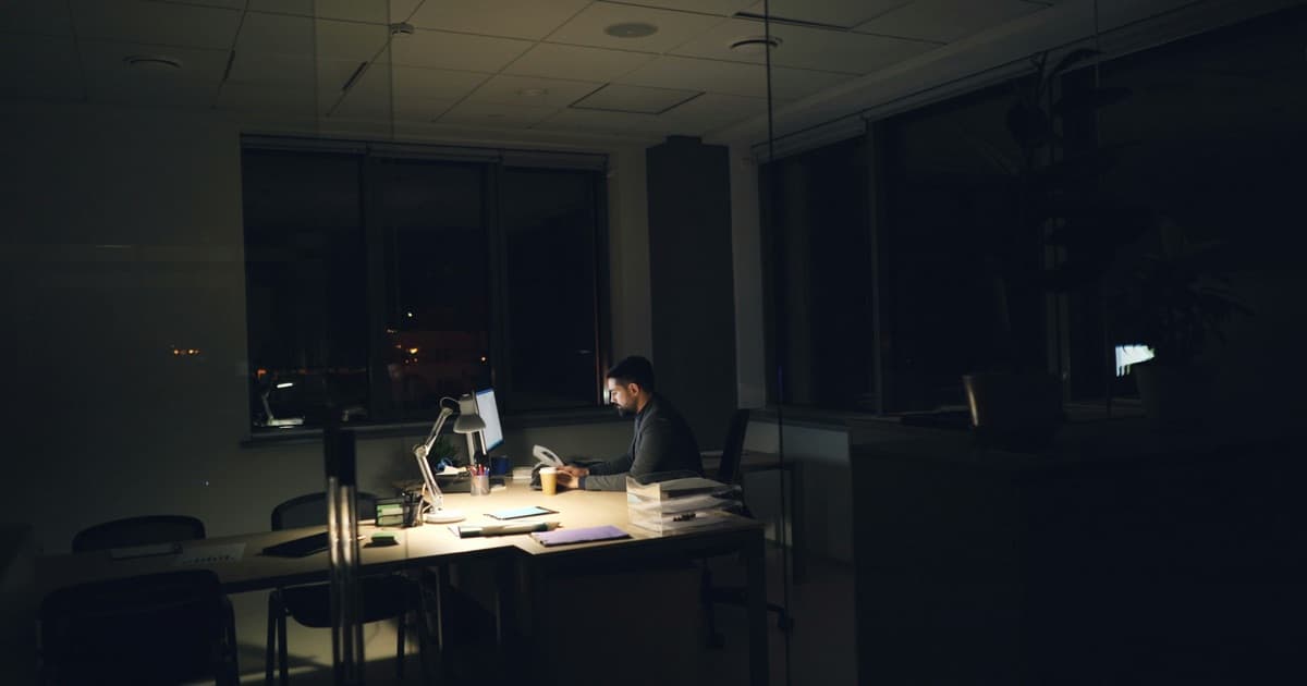 Homem trabalhando até tarde numa mesa de escritório com luz baixa, simbolizando o custo invisível das horas extras na gestão manual de hóspedes